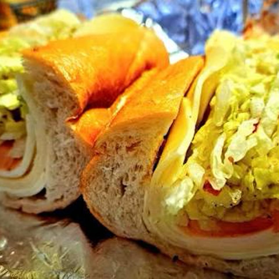 Two halves of a deli sub sandwich with lettuce, tomato, and cheese on foil.