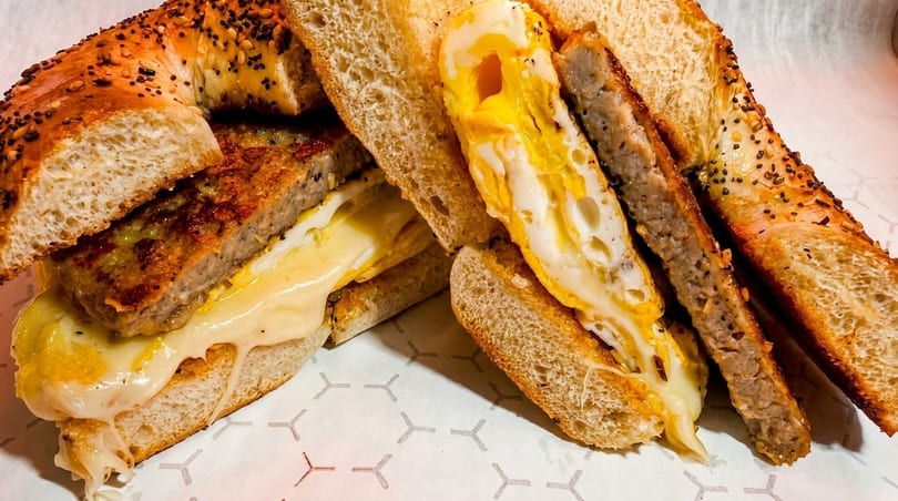 A breakfast sandwich with sausage, egg, and melted cheese on a toasted everything bagel.