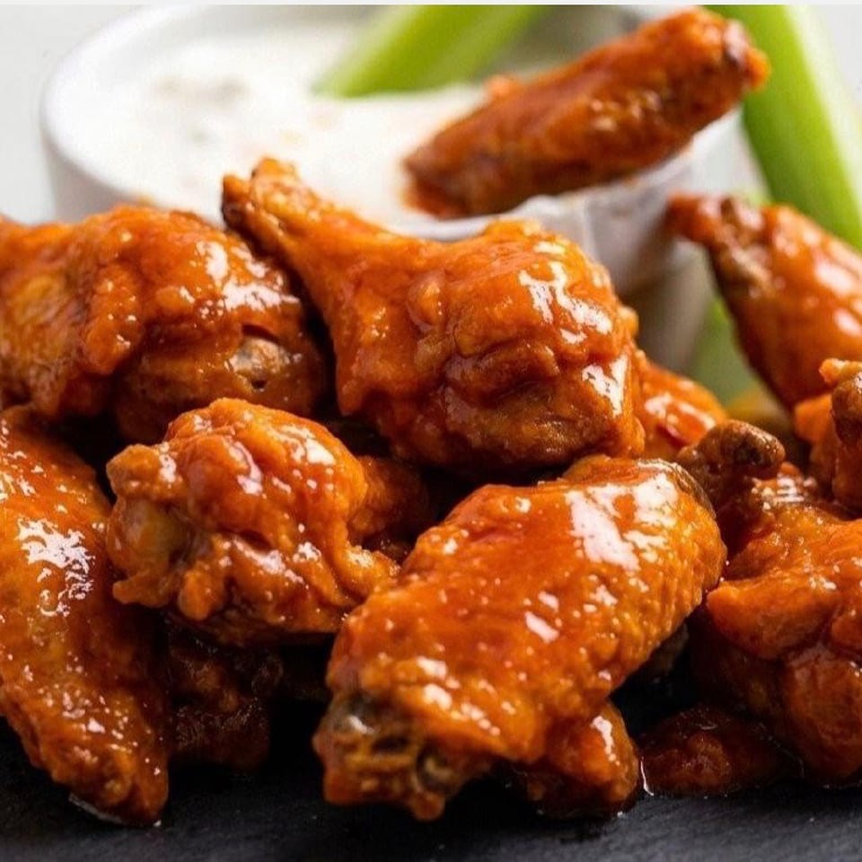 A close-up of a pile of buffalo chicken wings with ranch dressing and celery sticks.