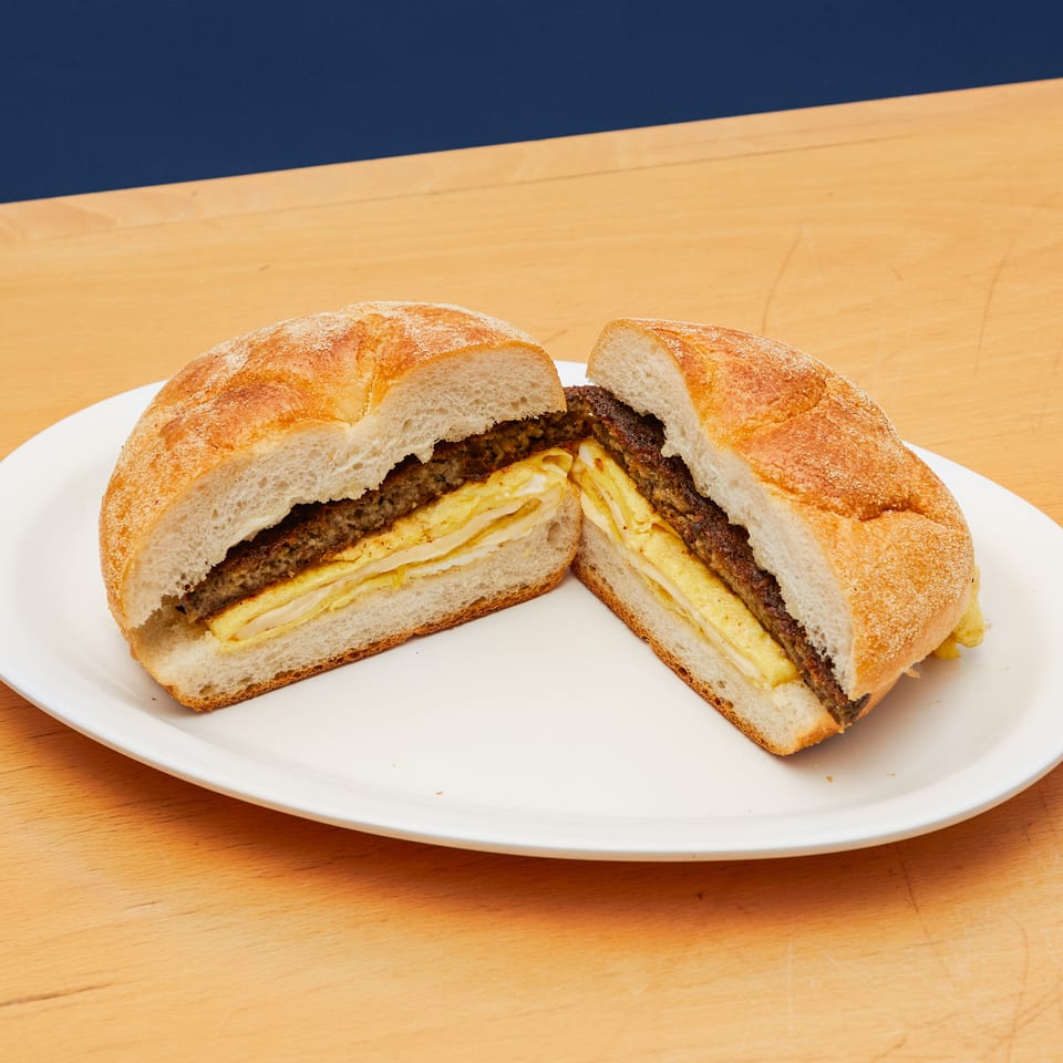 A sandwich with a dark patty and layered egg, cut in half on a white plate.