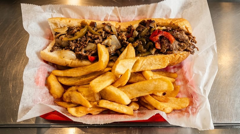 Cheesesteak sandwich with peppers and onions, served with a side of golden french fries.