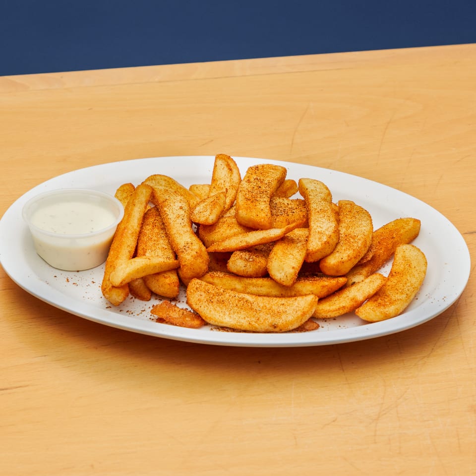 Golden seasoned potato wedges on a white plate with a side of creamy dipping sauce.