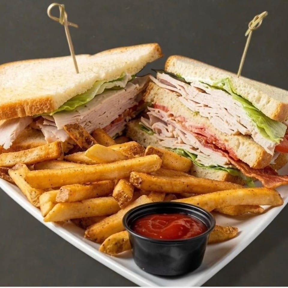 A club sandwich with turkey, bacon, lettuce, and tomato, served with a side of fries and ketchup.