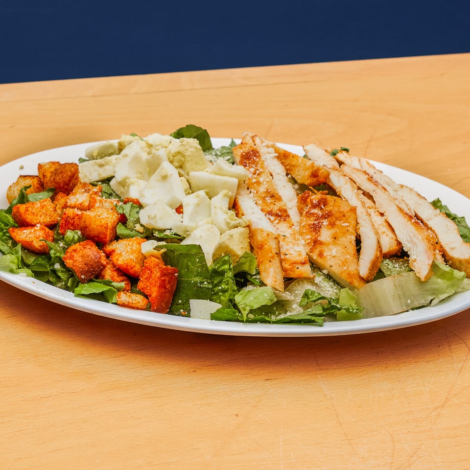A large salad with sliced grilled chicken, seasoned croutons, and chopped eggs on a white plate.