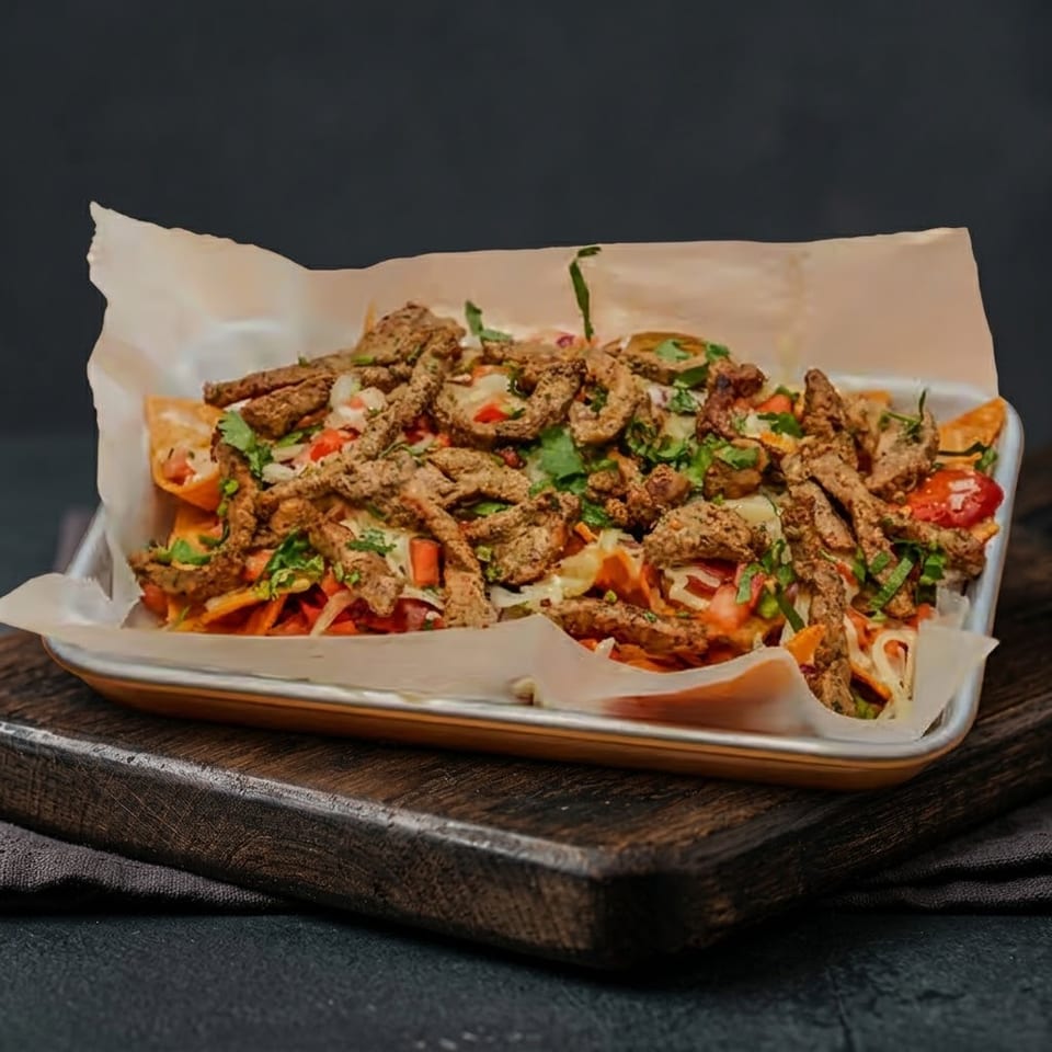 A tray of loaded nachos with meat, cheese, and vegetables on a wooden board.