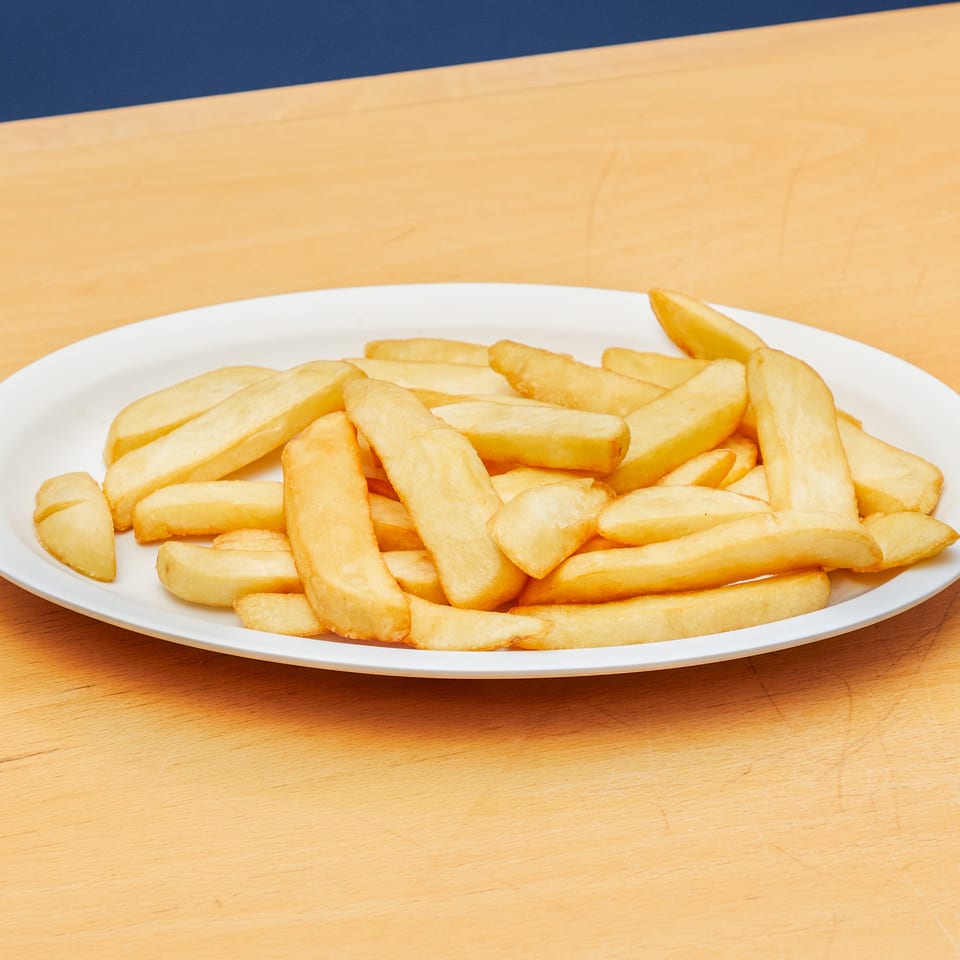 Golden, thick-cut french fries piled on a white oval plate on a light wooden surface.